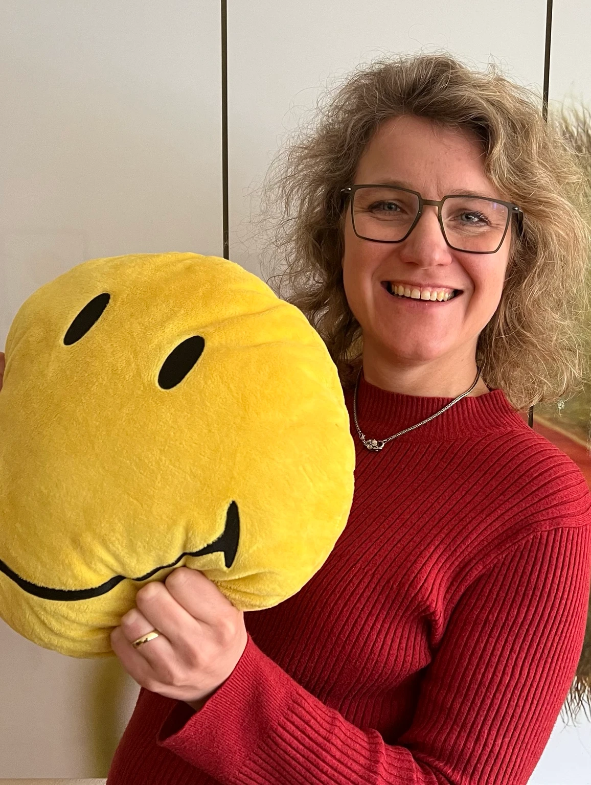 Angelika Düser lacht und hält ein großes Smiley-Kissen