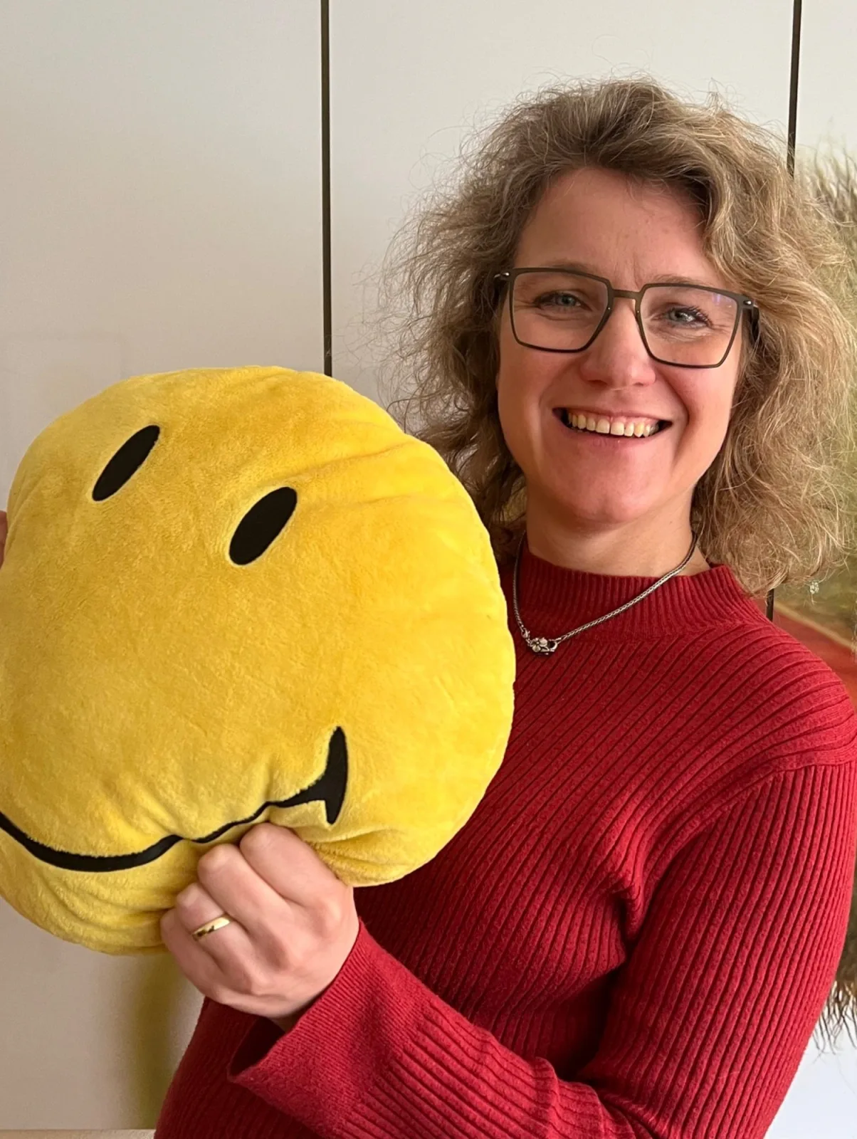 Angelika Düser hält lächelnd ein gelbes Smiley-Kissen